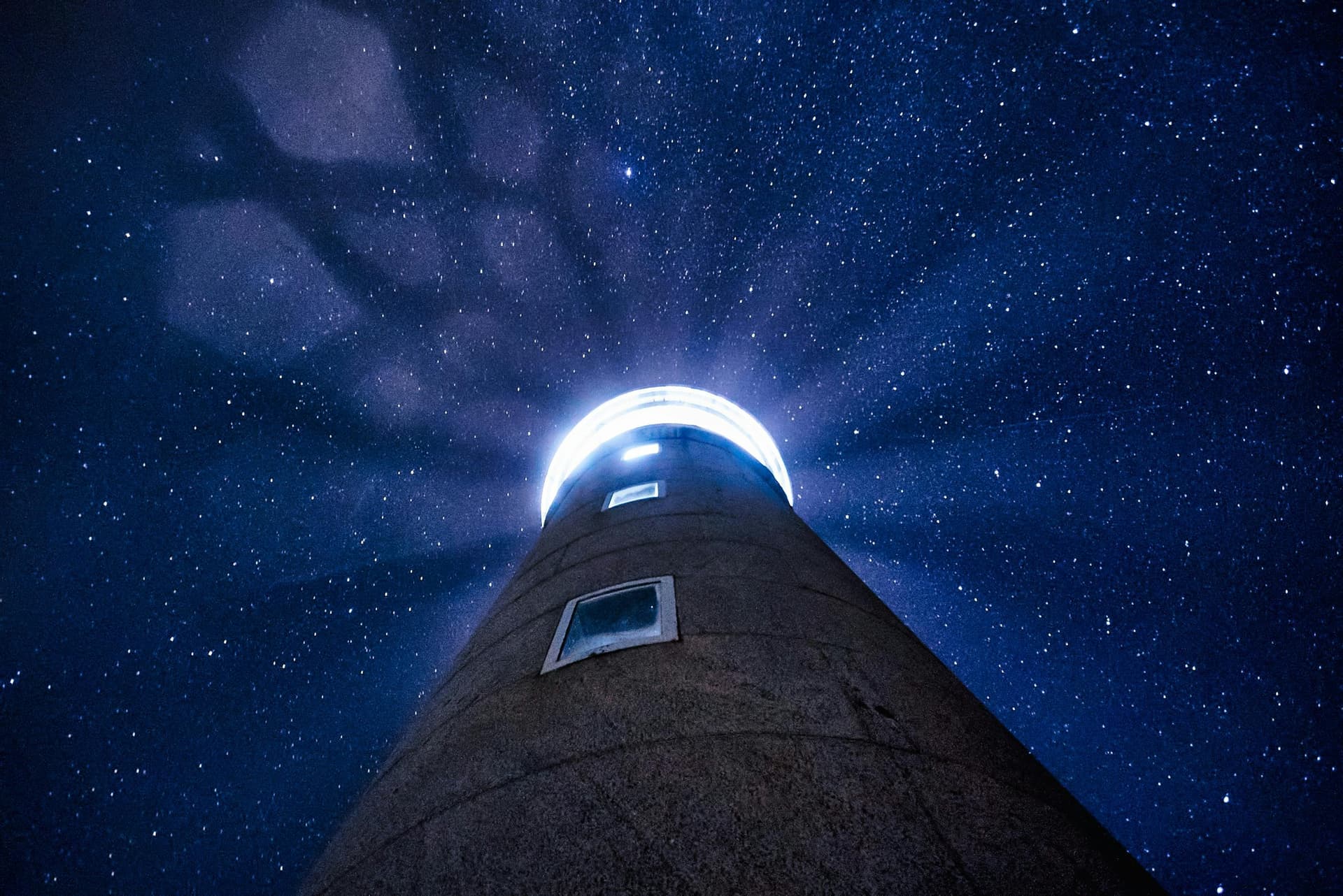 View upward from a tall tower into a star-filled night sky, with a bright ring of light near the top.