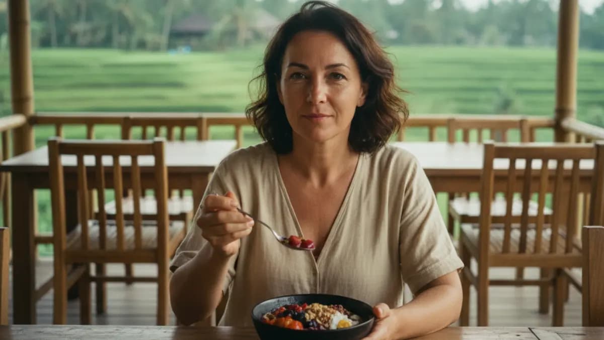 a middle aged modern woman of turkish descent sitting in a beautiful open-air restaurant surrounded by lush green rice paddies in Ubud, Bali, enjoying an acai bowl slowly and mindfully; soft tropical sunlight filtering through palm leaves, gentle breeze visible in her hair, symbolizing presence, gratitude, and mindful eating in harmony with nature